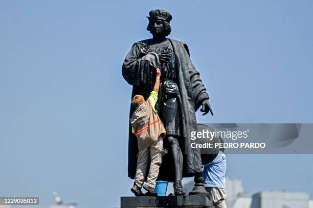 Municipal workers clean a statue of Christopher Columbus, which was protected by a metal fence after activists called to tear it down on social...