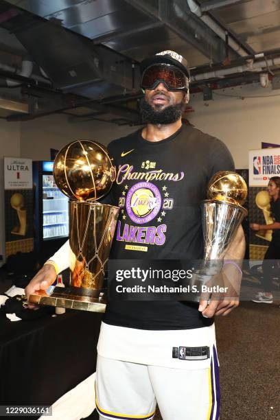 LeBron James of the Los Angeles Lakers holds the Larry O'Brien Trophy and The Bill Russell NBA Finals MVP Award in the locker room after winning Game...