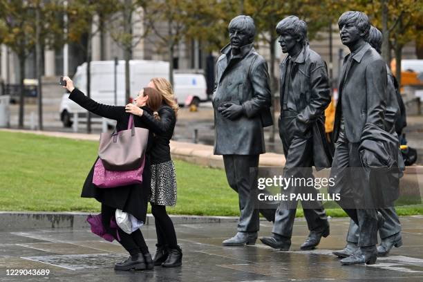 People pose with a statue of members of the Beatles, near the Liver Building in Liverpool, north west England on October 13 as new local lockdown...