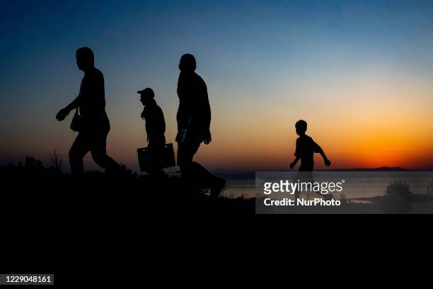 Silhouettes of walking refugees and migrants on the hills early in the morning during the dawn and the sunrise over the Aegean sea and Turkey. Asylum...