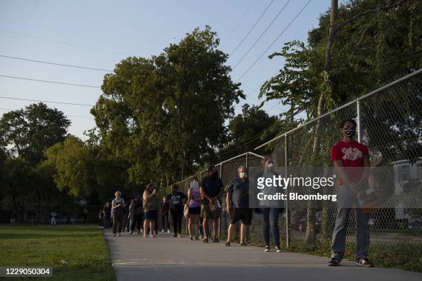 Voters wearing protective masks stand in a socially distanced line to cast ballots at an early voting polling location for the 2020 Presidential...