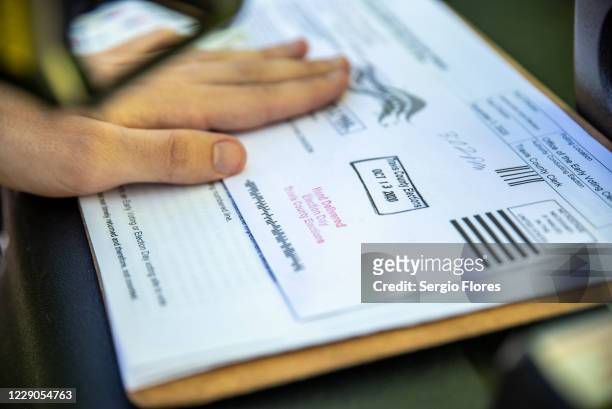 Poll worker stamps a voters ballot before dropping it into a secure box at a ballot drop off location on October 13, 2020 in Austin, Texas. The first...
