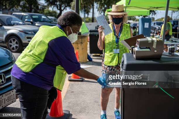 Workers drop voters ballots into a secure box at a ballot drop off location on October 13, 2020 in Austin, Texas. The first day of voting saw voters...