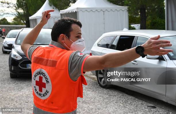 Member of the French Red-Cross wearing a face masks guides cars at a drive-through Covid-19 screening site on October 14, 2020 in Montpellier. -...