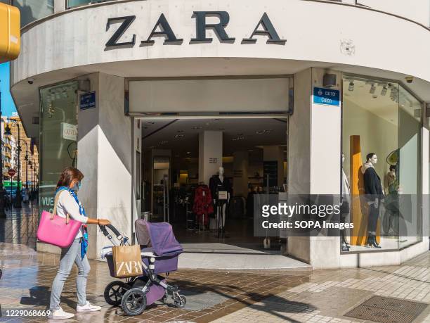 Woman wearing a face mask with a baby carriage and a Zara shopping bag walks past the Zara store.
