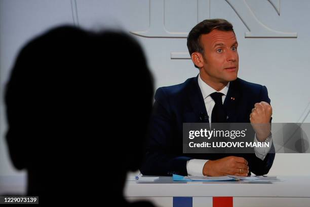 This picture shows a man watching a screen displaying French President Emmanuel Macron as he addresses the nation during a televised interview from...