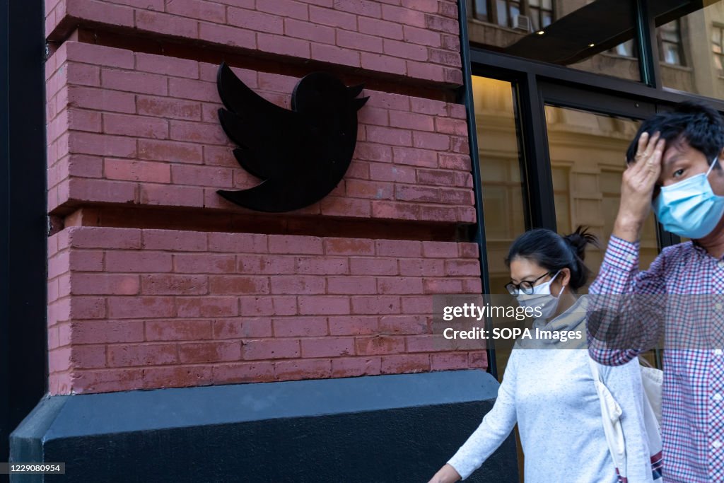 People wearing face masks walk past a Twitter logo outside...