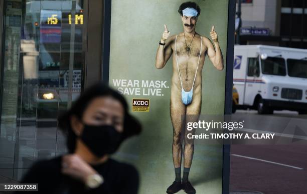 Person wearing a mask walks past a bus stop ad on 5th Avenue, October 15 for the upcoming movie "Borat 2," featuring actor Sacha Baron Cohen, ahead...