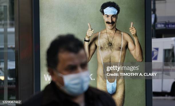 Person wearing a mask walks past a bus stop ad on 5th Avenue, October 15 for the upcoming movie "Borat 2," featuring actor Sacha Baron Cohen, ahead...