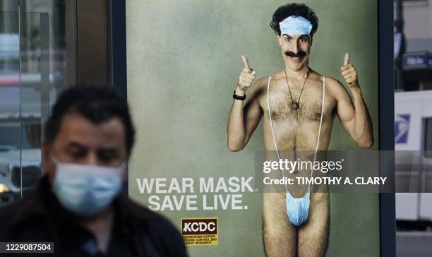 Person wearing a mask walks past a bus stop ad on 5th Avenue, October 15 for the upcoming movie "Borat 2," featuring actor Sacha Baron Cohen, ahead...