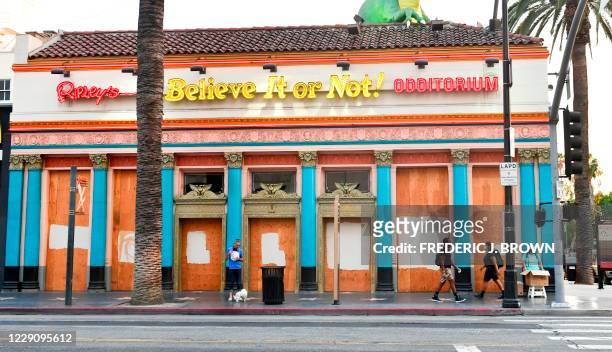 Pedestrains walk past a boarded up and temporarily closed Ripley's Believe It Or Not Museum on Hollywood Boulevard, closed due to the coronavirus...