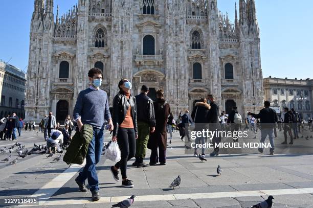 People wearing protective masks walk across the Piazza del Duomo in Milan on October 17 amid the Covid-19 pandemic. - Italy's government has made it...