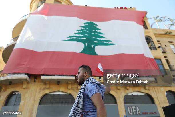 Man walks past a building covered with a giant Lebanese flag on the one-year anniversary of anti-government protests on October 17, 2020 in Beirut,...