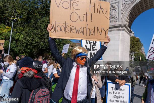 Protester dressed in a Trump costume holds a placard expressing his opinion at Washington Square Park during the demonstration. Thousands took to the...