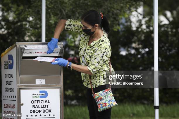 An election official wearing a protective mask and gloves places a mail-in ballot in a drop box at an early voting polling location for the 2020...