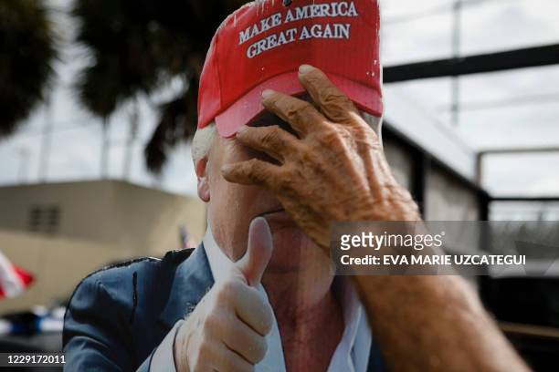 Hand holds a placard depicting US President Donald Trump's face outside John F. Kennedy Public Library as voters cast their early ballots in Hialeah,...