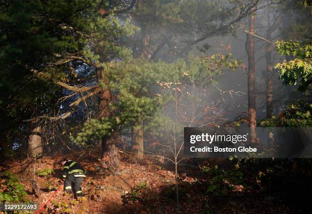 Firefighter heads down an embankment to grab a hose from his firetruck as crews work to put out a brush fire off of Elm Street in Medford, MA on Oct....