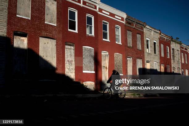 Man rides a bike past boarded up row houses in the Broadway East neighborhood on October 14 in Baltimore, Maryland. - Demon Lane says his east...