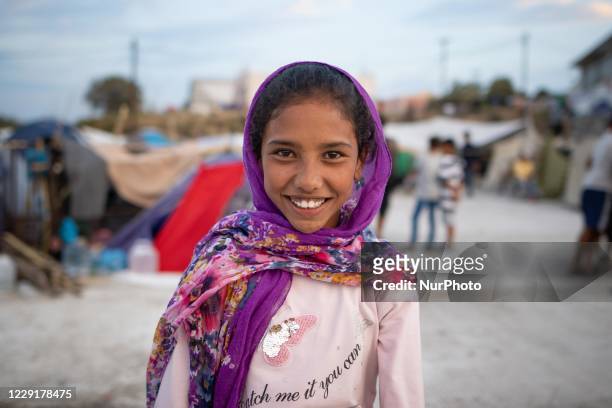Smiling girl with a headscarf at the roof of a building where she lived after the fire. Portraits of young children refugees, minors boys and girls,...