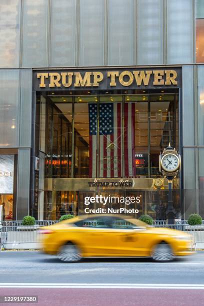 Taxi is passing in front of the main entrance of Trump Tower with the inscription on it and a US flag. Trump Tower in New York city in the USA. The...