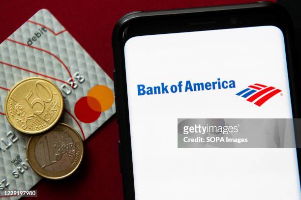 In this photo illustration a Bank of America logo seen displayed on a smartphone next to a debit card and two euro coins.