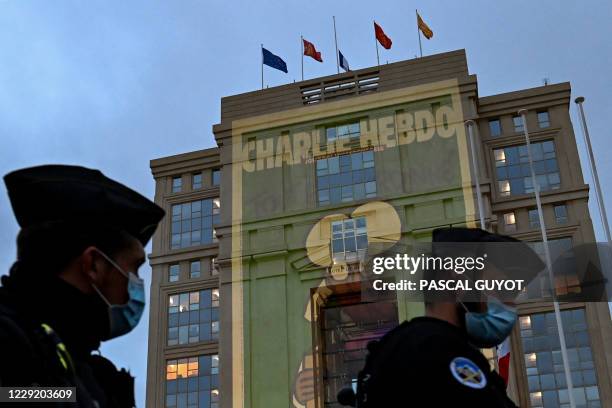 Police officers walk past cartoons of French satirical weekly newspaper Charlie Hebdo projected onto the facade of the Hotel de Region in...