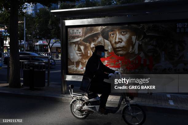 Man rides past a poster for the movie "Sacrifice", about China's entry into the 1950-1953 Korean War to fight alongside North Korea against the US,...