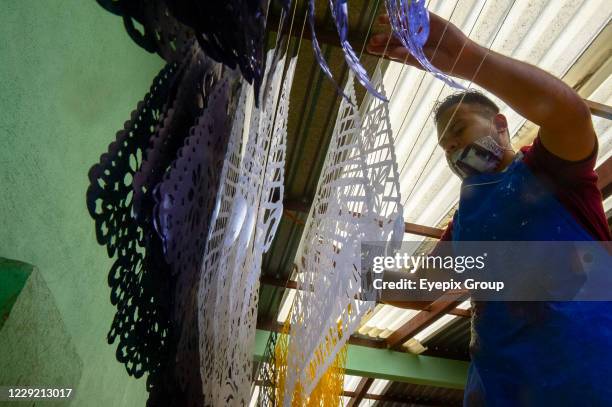 Worker from the "Taller de Yuriria" wears a protective mask, while holds a Mexican cut paper 'Papel Picado', that is used to decorate offerings and...