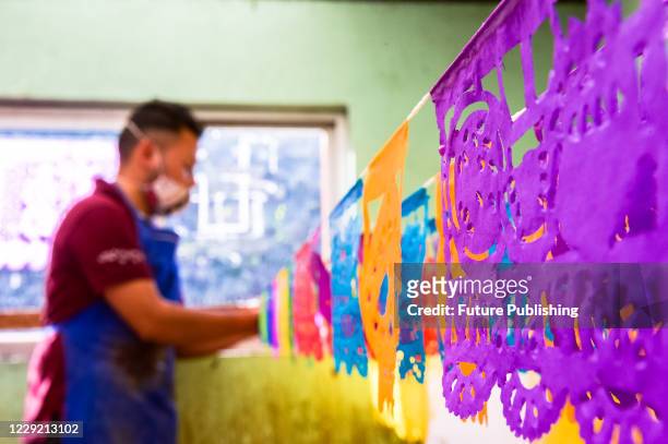 Worker from the "Taller de Yuriria" wears a protective mask, while holds a Mexican cut paper 'Papel Picado', that is used to decorate offerings and...