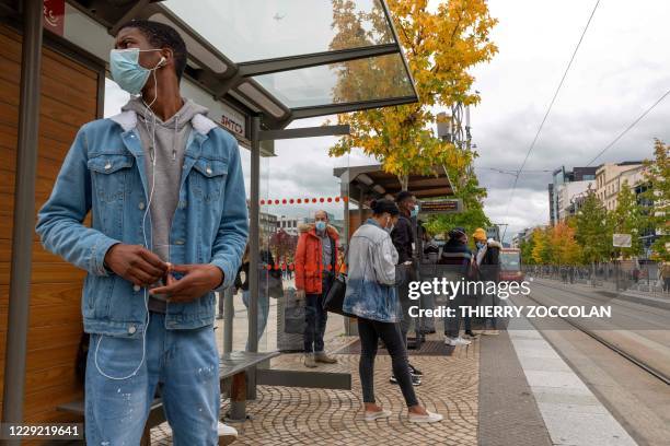 Two men, wearing face masks, wait for a tram, Place de la Jaude, in Clermont-Ferrand, as French Prime Minister holds a press conference on Covid-19...