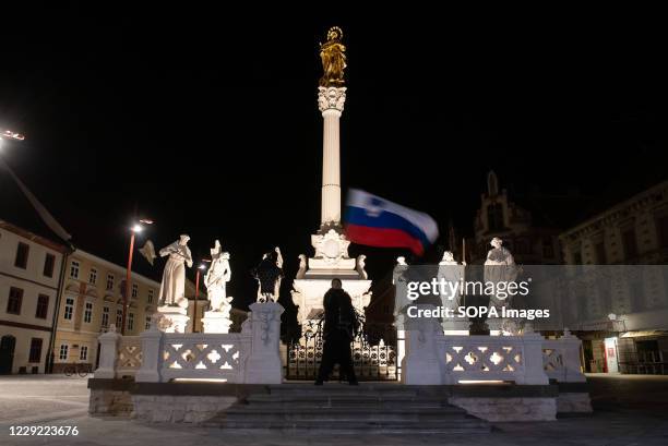 Protester against the night curfew enforcement and lockdown restrictions waves the Slovenian flag infront of the Plague Column past the night curfew...