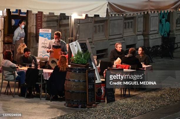 People enjoy drink and food in bars at a terrace in the Navigli district in southern Milan on October 22 before the closing of the sites. - Lombardy...