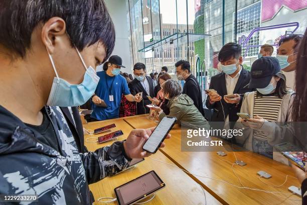 People try out the new iPhone 12 mobile phones at an Apple store in Shanghai on October 23, 2020. / China OUT
