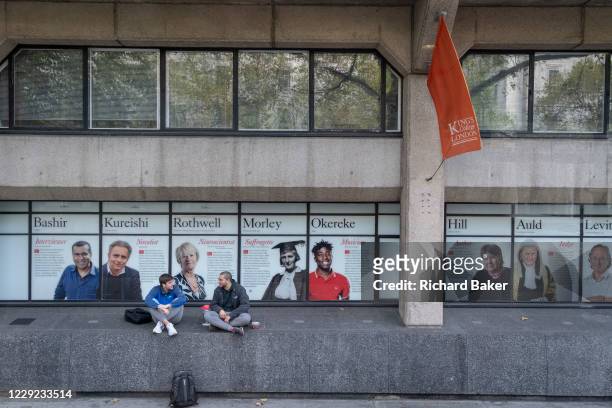 Two young men talk on a wall near the faces of past alumni a wall outside King's College London University on the Strand, during the second wave of...