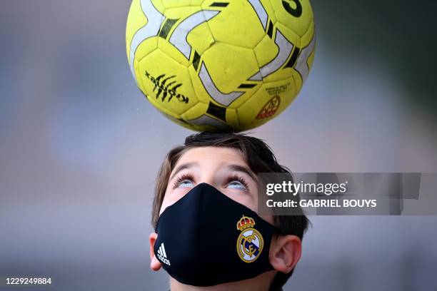 Boy wearing a face mask to protect against the spread of the novel coronavirus juggles with a ball prior to a football match with his team of...