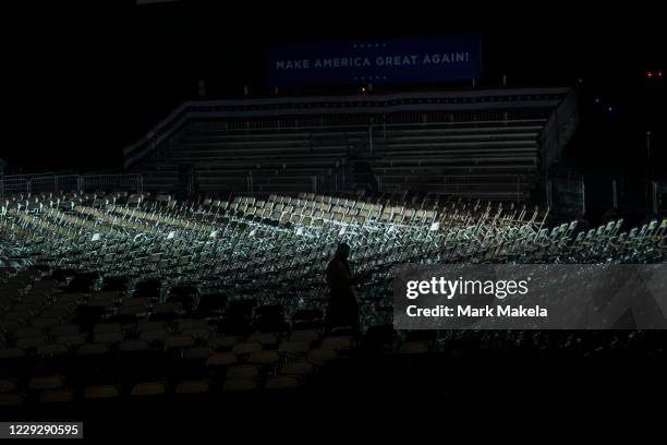 Member of campaign staff walks through empty rows of seats below a "MAKE AMERICA GREAT AGAIN" banner pre-dawn before President Donald Trump holds a...