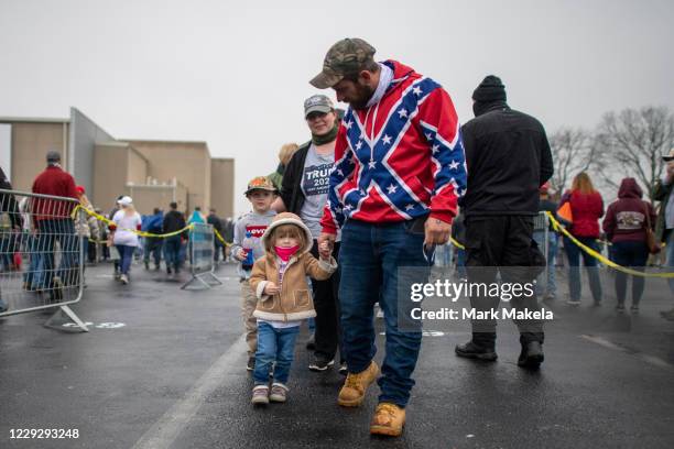 Man wearing a Confederate flag themed sweatshirt walks with his children while queueing before President Donald Trump holds a rally on October 26,...