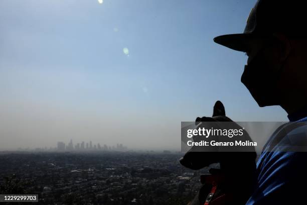 Anthony Bravo and his dog Kylo watch as smoke from the Silverado fire in Orange County shrouds the Los Angeles skyline as seen from the Griffith...