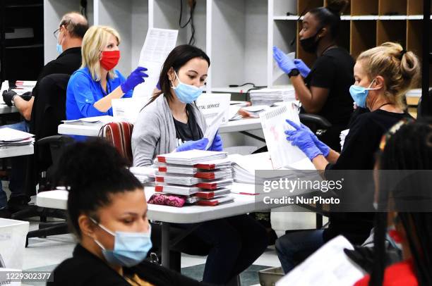 Election office workers wear face masks and gloves as they process mail-in ballots in the ballot duplicating room at the Orange County Supervisor of...