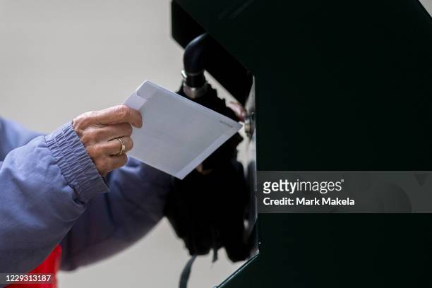 Voter deposits their ballot in an official ballot drop box while a long line of voters queue outside of Philadelphia City Hall at the satellite...