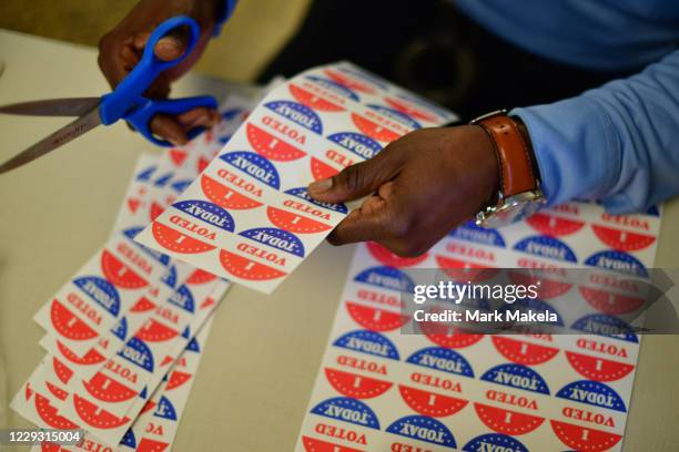 Volunteer cuts out " I VOTED TODAY" stickers for voters queueing outside of a satellite polling station on October 27, 2020 in Philadelphia,...