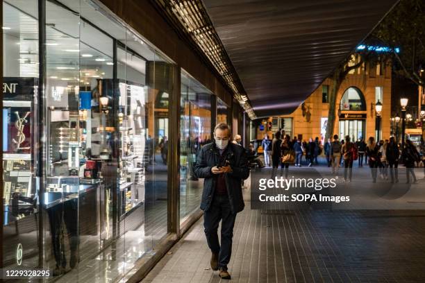 Man wearing a facemask is seen using his mobile phone past the Corte Inglés shopping center in Plaza Catalunya with less than an hour before start of...