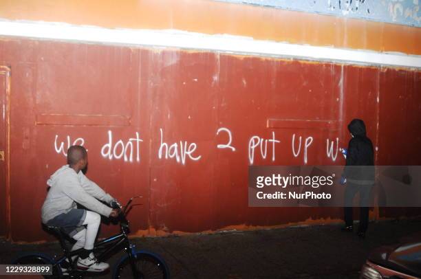 White protester sprays graffiti across a wall in West Philadelphia as a neighborhood kid rides past on his bike, highlighting a chief compliant from...