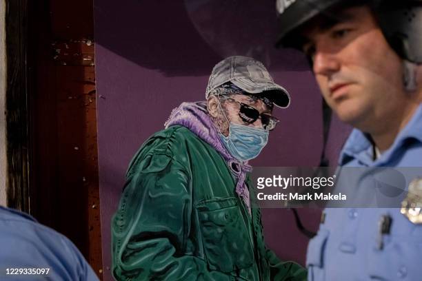 Mural depicting a person wearing a mask is seen behind police officers congregating an hour before a citywide curfew, on October 28, 2020 in...
