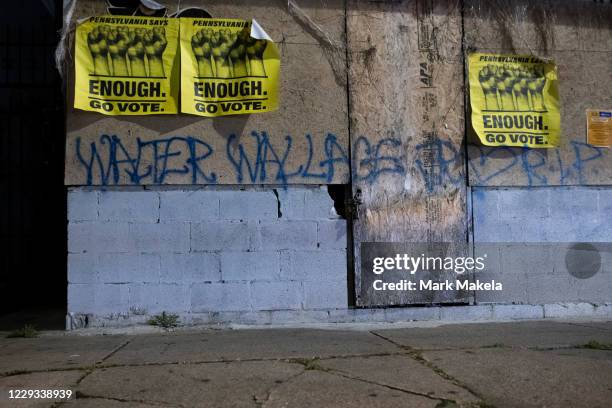 Car headlights illuminate posters reading "ENOUGH GO VOTE" and graffiti stating "WALTER WALLACE RIP" during a citywide curfew on October 28, 2020 in...