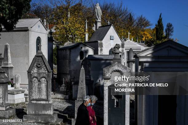 Two women wearing face masks walk past tombs and vaults at the Alto de Sao Joao cemetery in Lisbon on October 30, 2020 on the eve of All Saints' Day...