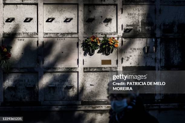 Woman wearing a face mask walks past a columbarium at the Alto de Sao Joao cemetery in Lisbon on October 30, 2020 on the eve of All Saints' Day amid...