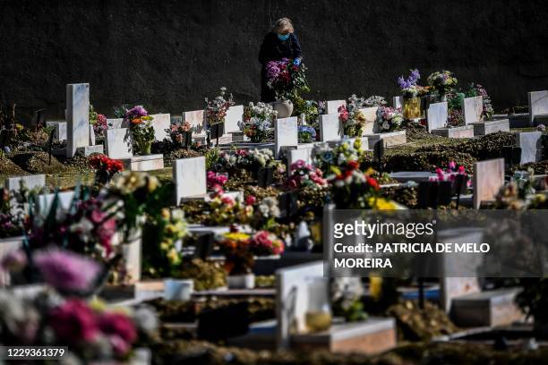 Woman wearing a face mask puts flowers at the tomb of a relative at the Alto de Sao Joao cemetery in Lisbon on October 30, 2020 on the eve of All...