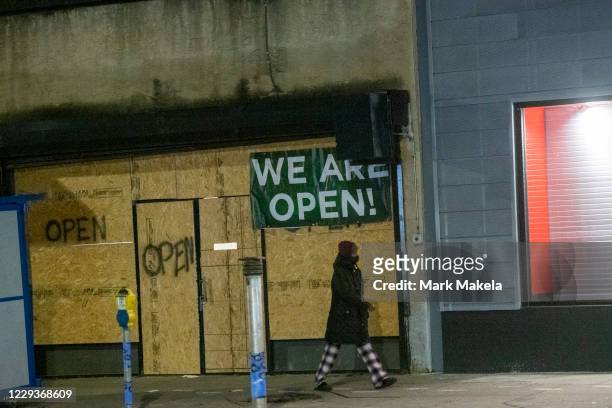 Woman walks past a boarded up store with a draped banner and spray painted "OPEN" notices after looting on October 30, 2020 in Philadelphia,...