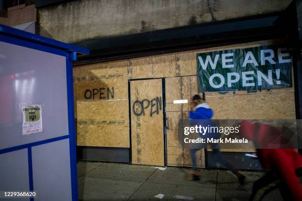 Women run past a boarded up store with a draped banner and spray painted "OPEN" notices after looting on October 30, 2020 in Philadelphia,...